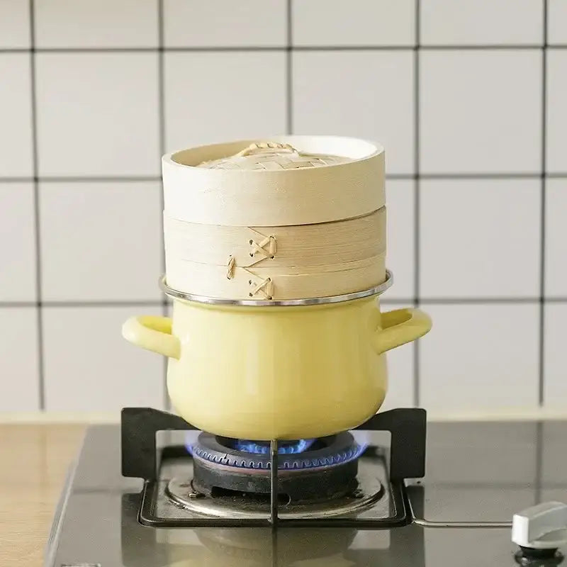 A two-tiered bamboo steamer sits atop a pale yellow enamel stock pot with gold clasps on a gas stove