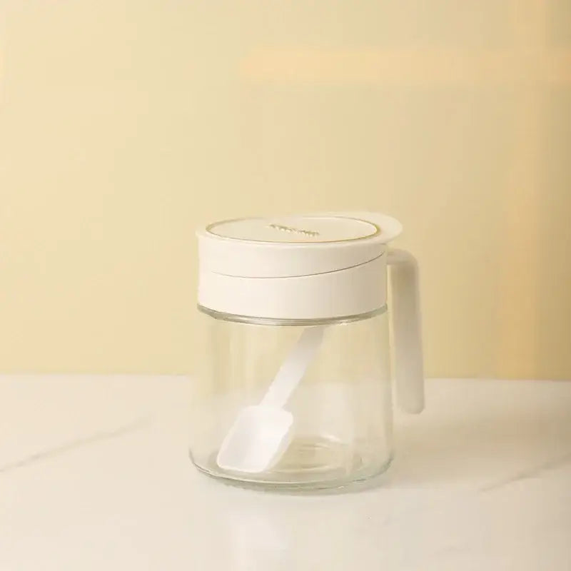 Clear glass seasoning jar with white lid handle and integrated spoon for kitchen spice shaking and storage