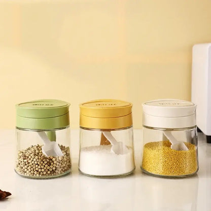 Set of three clear glass seasoning jars with green yellow and white lids each containing a plastic scoop spoon
