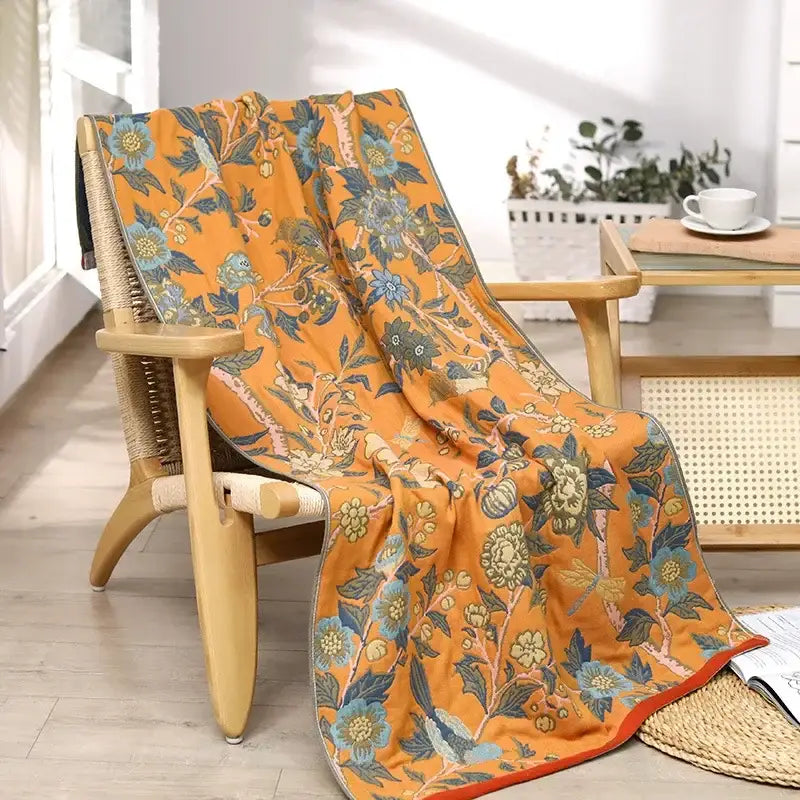 Orange floral-patterned cotton large bath towel with blue and green blossoms draped over a wooden chair for bathroom decor