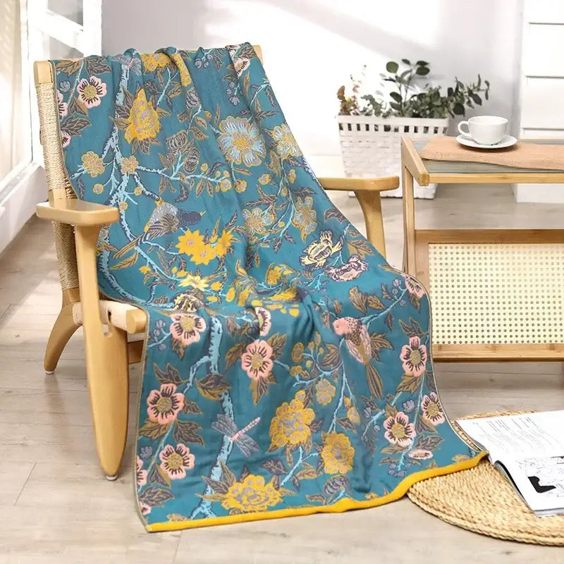 Teal cotton large bath towel with yellow and pink blossoms, birds, and dragonflies draped over wooden chair