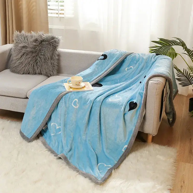 Light blue plush cartoon flannel blanket with gray border and heart patterns by decorbites draped over a sofa
