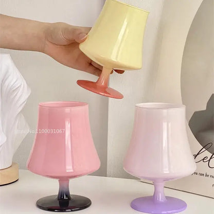 A hand holds a pastel yellow and coral decorbites gem champagne coupe glass with glossy finish beside gradient glasses