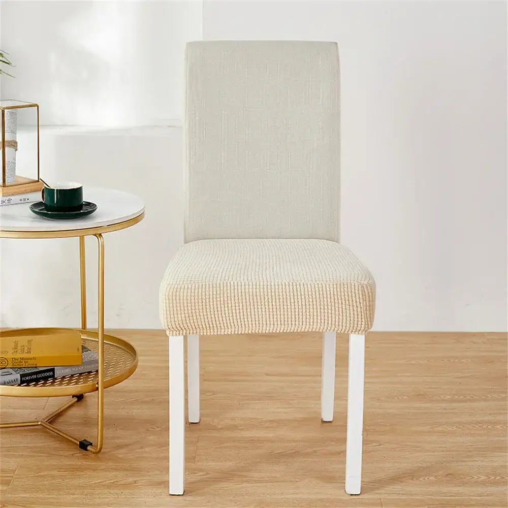 Beige fleece chair cover with subtle woven pattern snugly fitted over white dining chair for seat protection