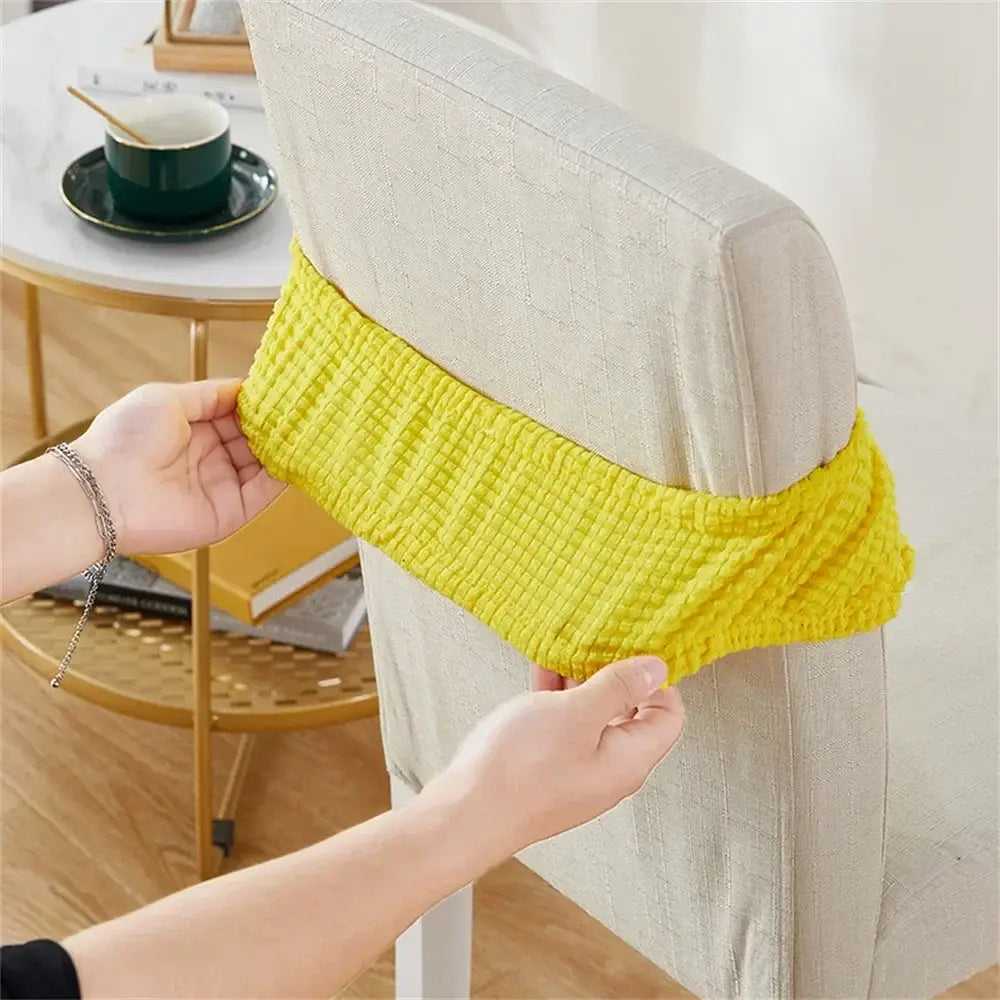 Bright yellow ribbed fleece chair cover being fitted over the back of a light beige upholstered dining chair