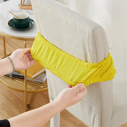 Bright yellow ribbed fleece chair cover being fitted over the back of a light beige upholstered dining chair