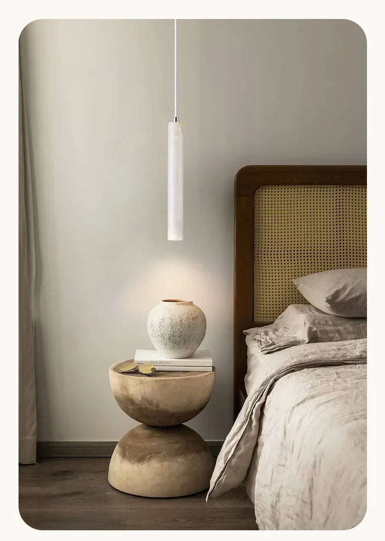 A minimalist white stone pendant light with a sleek cylindrical design hanging in a bedroom setting