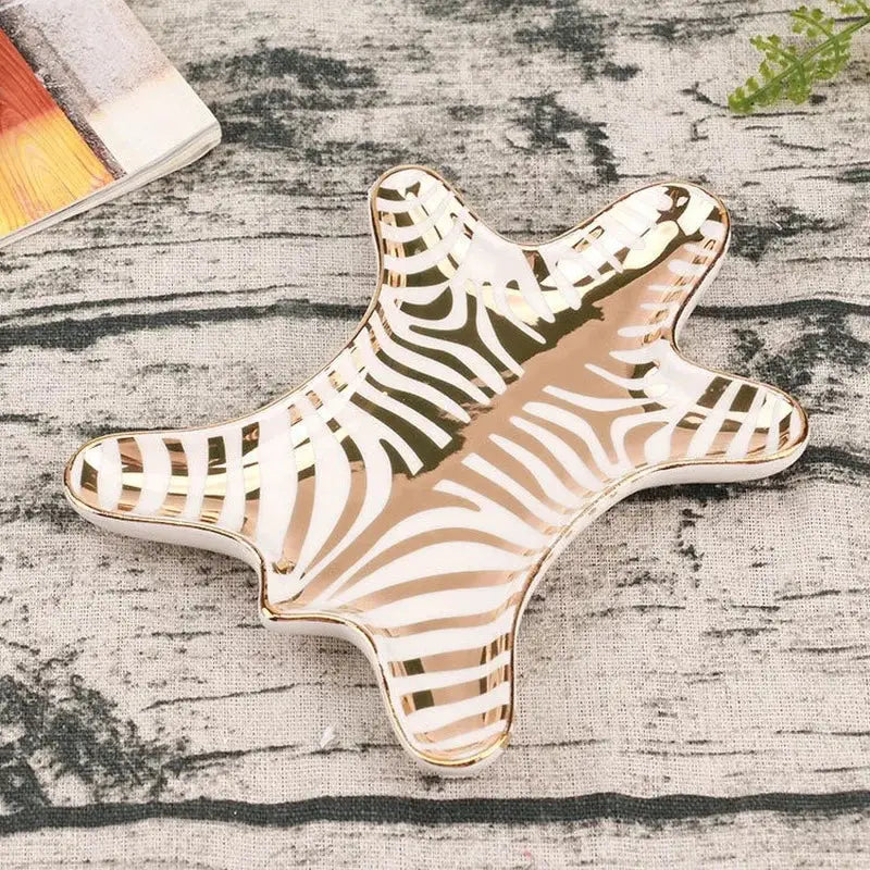 A glossy ceramic jewelry holder tray shaped like a starfish with white and gold tiger skin stripes and a gold rim