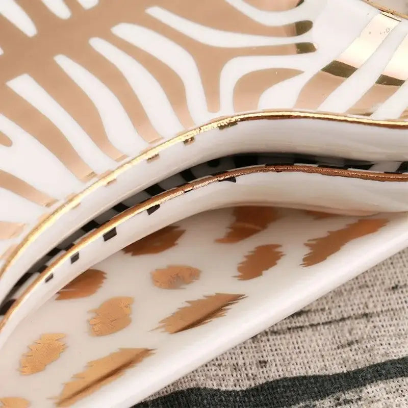 A white ceramic jewelry holder tray with gold tiger skin zebra stripe and feather motifs edged in shiny gold trim